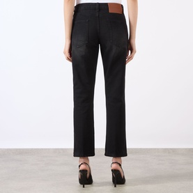 Model wearing Victoria Beckham Washed Black straight-leg jeans, rear view, styled with black heeled mules, tan leather patch detail visible.