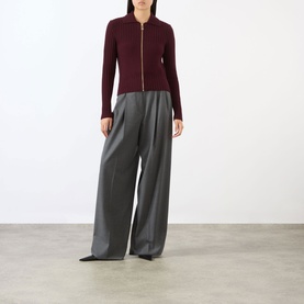 Model wearing Victoria Beckham Zip Knitted Polo Sweater in Acai with gold-tone zip, styled with wide-leg grey trousers and black pointed heels.