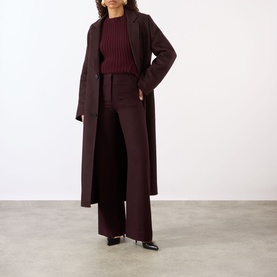 Model wearing a longline burgundy wool coat styled with matching ribbed jumper, wide-leg trousers and black heeled boots
