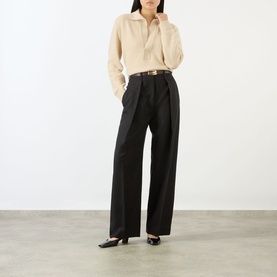 Model wearing Victoria Beckham Elderflower knit polo, styled with wide-leg black trousers, brown belt, and black flat mules.
