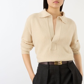 Model wearing Victoria Beckham knit polo in Elderflower, styled with dark wide-leg trousers and a brown leather belt with gold buckle.