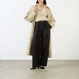 Model wearing Victoria Beckham Elderflower knit polo, styled with beige trench coat, wide-leg black trousers and black heels.