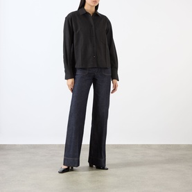 Model wearing black long-sleeve collared shirt with button front, styled with wide-leg dark indigo jeans and black flat shoes