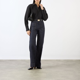 Model wearing dark indigo wide-leg jeans with black shirt, styled with black shoulder bag and square-toe flats