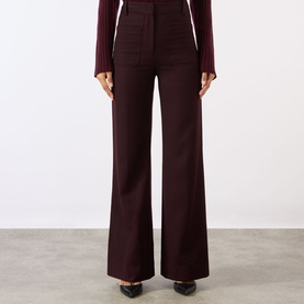 Model wearing Victoria Beckham Alina High-Rise Wide Leg Trousers in Acai, styled with a dark knit top and black heels
