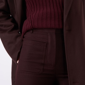 Model wearing Victoria Beckham Alina High-Rise Wide Leg Trousers in Acai, close-up of rear patch pocket, styled with matching blazer and ribbed knit