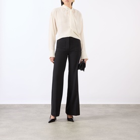 Model wearing Victoria Beckham black wide-leg trousers, styled with a cream blouse, black clutch bag and black heels.