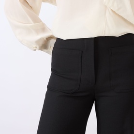 Model wearing Victoria Beckham black trousers with front patch pockets, styled with a cream blouse.