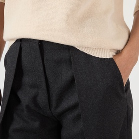 Model wearing Victoria Beckham dark grey melange trousers with front pleats and side pockets, styled with a cream knit top.