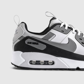 Nike Air Max 90 trainer in vast grey and white with black mesh upper, grey swoosh, and visible Air cushioning unit on sole