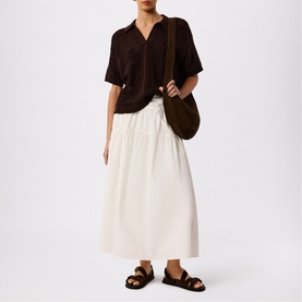 Model wearing Whistles brown short-sleeve shirt, styled with white midi skirt, brown sandals, and a brown shoulder bag.