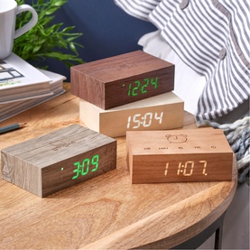 Gingko flip click clocks in dark walnut and light wood finishes displaying green LED time, shown grouped on a bedside table
