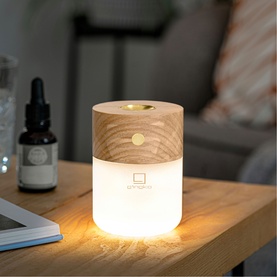 Aroma diffuser with light wood grain top and glowing white base, styled on a wooden side table with essential oil bottle
