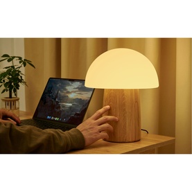 Gingko mushroom table lamp with warm glowing dome shade and oak-effect base, styled on a wooden desk beside a laptop