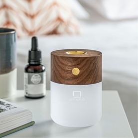 Gingko lamp with walnut wood finish and white frosted base, glowing warm light, styled on a bedside table with essential oil bottle