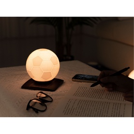 Gingko football-shaped white LED table lamp glowing on a desk beside glasses, a phone and an open book in a dimly lit room