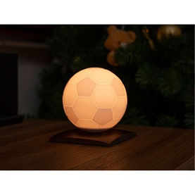 Gingko football-shaped table lamp in warm white glow, seated on a dark wooden base, shown in dim ambient lighting.