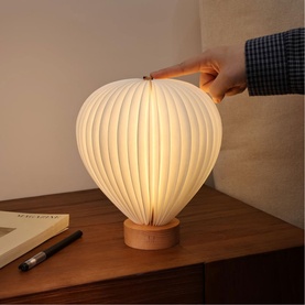 Gingko ribbed white balloon table lamp with wooden base, hand adjusting the top, glowing warmly on a wooden sideboard