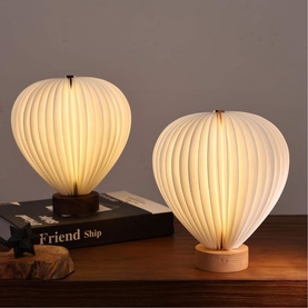 Gingko ribbed hot-air balloon table lamps in cream white with wooden bases, shown in two sizes on a wooden surface
