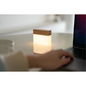 Small glowing white lamp with bamboo top, on a desk beside a laptop, with a hand typing in the background
