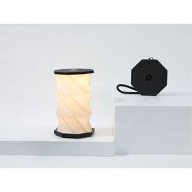 Gingko Mini Slate Black portable lamp, glowing white twisted cylindrical shade with black trim, shown assembled and flat-packed