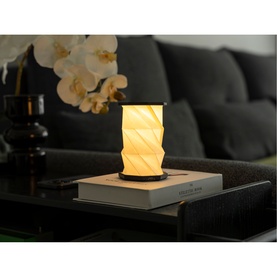 Gingko Mini Slate Black portable lamp glowing on a coffee table book, styled with white orchids and dark sofa in background