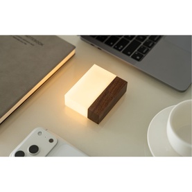 Small rectangular ambient lamp with warm white glow, dark walnut wood base and frosted acrylic top, styled on a desk with laptop and coffee cup