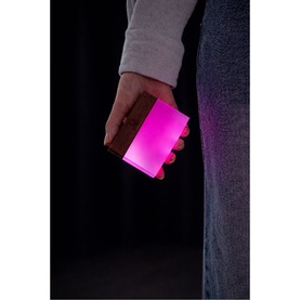 Hand holding a glowing pink rectangular portable light against a dark background