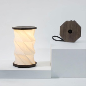 Gingko Mini Walnut Drift portable lamp, two views: glowing twisted white shade with dark wood base, and flat-packed octagonal form with loop handle