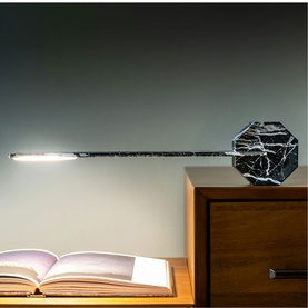 Gingko Black Marble desk lamp with extended slim arm, illuminated, styled on wooden cabinet beside open book