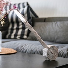 Gingko geometric wooden desk lamp in grey-toned wood finish, angled on a black coffee table in a styled living room setting.