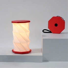 Gingko Mini Coral Red origami-style table lamp, illuminated white accordion shade with red base, shown with compact folded carry case