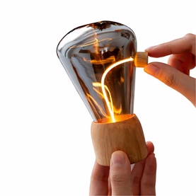 Smoked glass cordless LED table lamp with warm filament glow, on a natural wood base, shown being switched on by hand