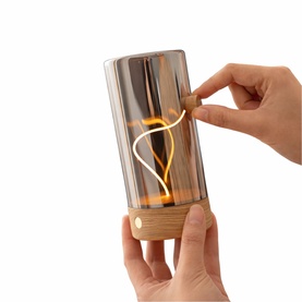 Cylindrical glass portable lamp with warm LED filament glow and oak wood base, shown being switched on by hand