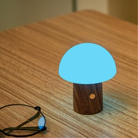 Small mushroom-shaped LED lamp with glowing blue dome and dark wood-effect base, styled on a wooden surface beside glasses