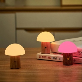 Three mushroom-shaped LED night lights with wooden bases, glowing warm white and pink, displayed on a desk beside stacked books