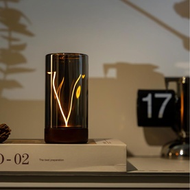 Gingko amber glass table light with cut-out botanical design, casting warm golden leaf shadows, styled on books beside a flip clock