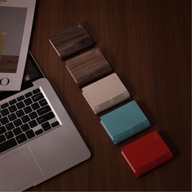 Gingko light in Walnut Finish alongside three colour variants in cream, teal and red, displayed on a wooden desk beside a laptop.
