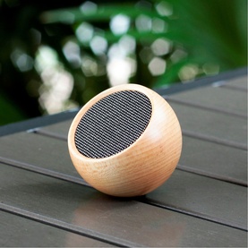 Gingko round portable Bluetooth speaker in natural wood finish with mesh grille, placed on a slatted surface outdoors