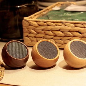 Gingko Mini Speaker trio in light and dark wood finishes, rounded form with metal mesh grille, styled on a wooden surface beside a wicker tray
