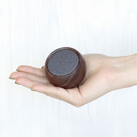 Gingko compact round wooden Bluetooth speaker with grey mesh grille, held in one hand to show small size