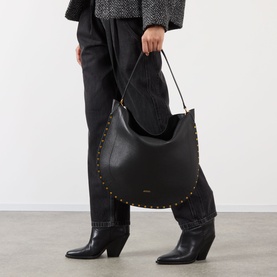 Model carrying Isabel Marant Oksan Hobo Shoulder Bag in black grained leather with gold-tone stud trim detailing, styled with black boots and trousers