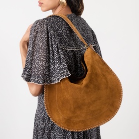Model carrying large tan suede hobo shoulder bag with whipstitch edge detailing, styled with a floral midi dress