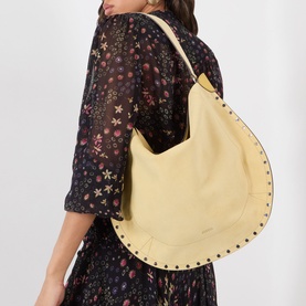 Model carrying Isabel Marant Oksan Hobo Shoulder Bag in straw, silver-tone studs around trim, worn over shoulder with floral dress