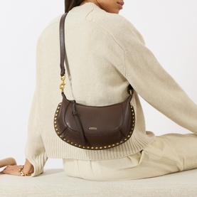 Model carrying Isabel Marant Oskan Moon Shoulder Bag in coffee leather with gold stud embellishment and adjustable strap, styled with cream knit