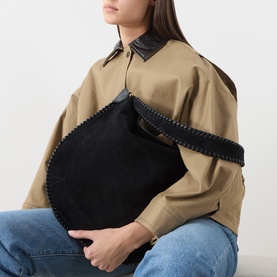 Model carrying Isabel Marant Oksan Hobo Shoulder Bag in black suede with braided trim and gold-tone hardware, styled with beige jacket and jeans