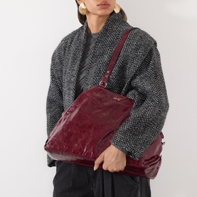 Model carrying Isabel Marant Winna Tote Bag in burgundy leather, slouchy silhouette with silver-tone hardware and shoulder strap, styled with grey