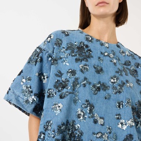 Model wearing Marques Almeida Sequin Embroidered Mini Denim Dress in mid blue, close-up showing floral sequin embroidery and short sleeves.