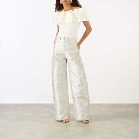 Model wearing Marques Almeida white wide-leg jeans with floral jacquard pattern, styled with a white ruffle bardot top and strappy heels