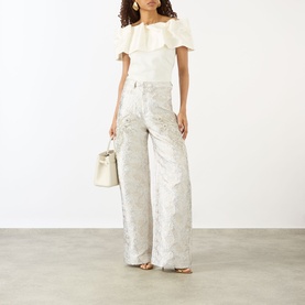 Model wearing Marques Almeida white wide-leg jacquard jeans, styled with off-shoulder ruffle top and carrying a cream bucket bag.